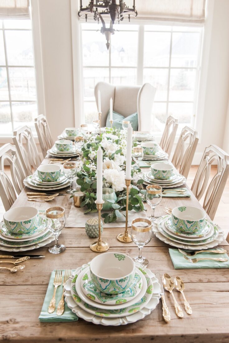 Vibrant spring-themed table setting with green, white, and gold dinnerware, lush floral centerpiece, and elegant candlesticks, perfect for festive gatherings or special occasions.