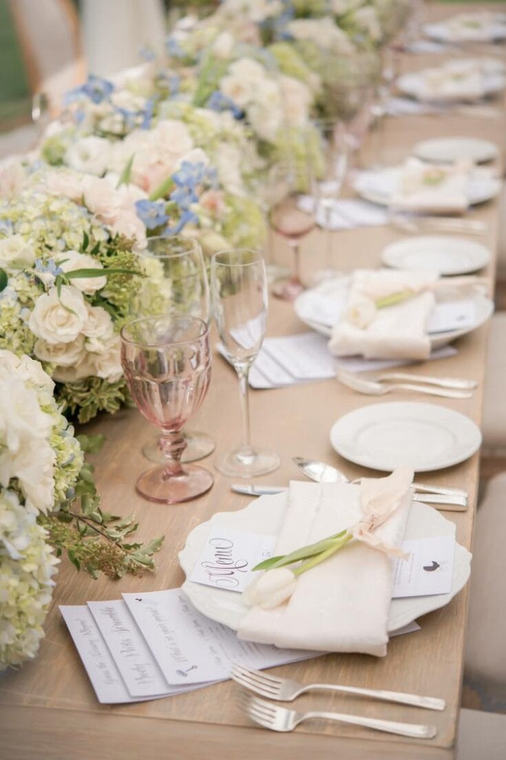 Elegant wedding table setting with floral arrangements, detailed place settings, and pastel-colored glassware, perfect for a romantic and sophisticated celebration.