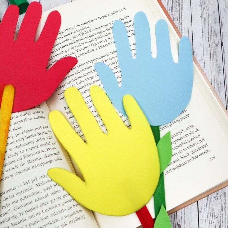 Handmade paper hands in red, yellow, and blue on open book about Rzym, symbolizing community and kindness, perfect for promoting positivity and educational activities related to charity and social awareness.