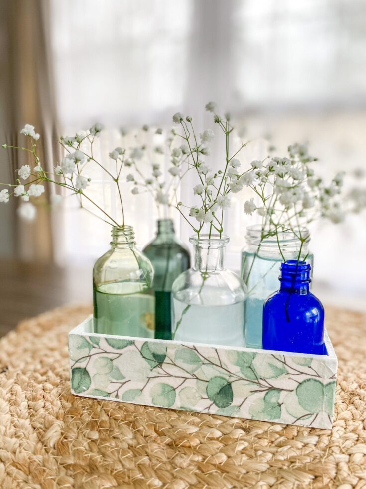 Colorful glass bottles with white baby's breath flowers in a decorative tray, showcasing elegant floral accents for home decor or wedding arrangements.