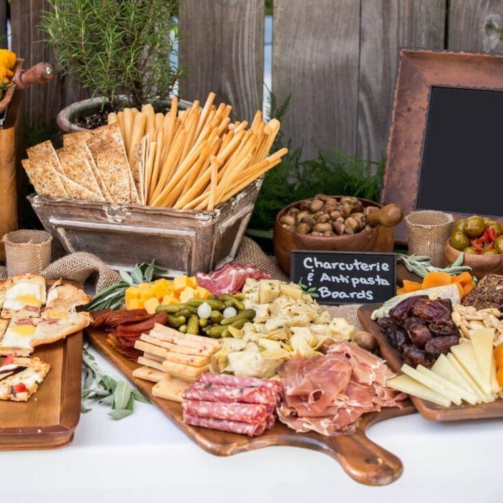 Assorted charcuterie and cheese platter with breadsticks, nuts, and vegetables, perfect for gatherings and celebrations, displayed on rustic wooden tables.