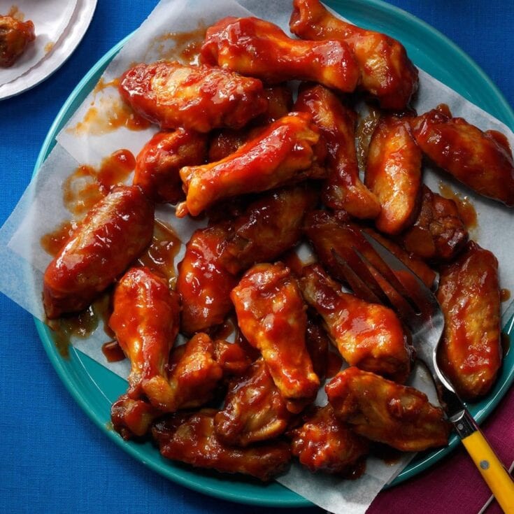 Juicy buffalo chicken wings coated in spicy, tangy sauce served on a teal plate with parchment paper and a fork, perfect for game day or casual gatherings.