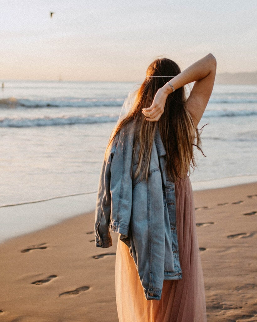 Sunset beach yoga woman, carefree and relaxed, wearing a denim jacket and flowy dress, enjoying peaceful seaside sunset, mindfulness, relaxation, boho lifestyle, peaceful beach scene, nature, coastal beauty.