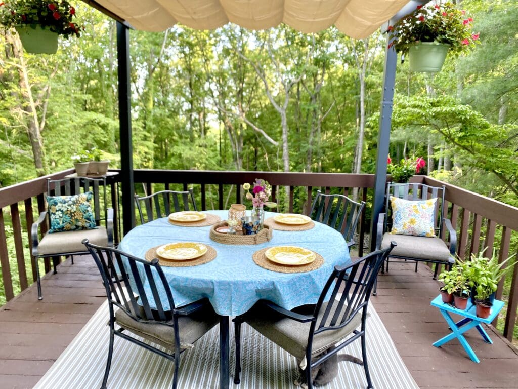 Wooden deck outdoor furniture, cozy porch dining area with table and chairs in lush green forest setting.