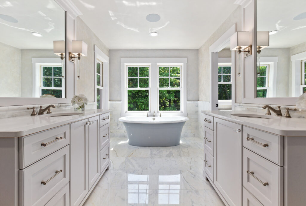 Luxurious white marble bathroom with double vanities, freestanding bathtub, bright natural light, and elegant decor for relaxation and spa experience.