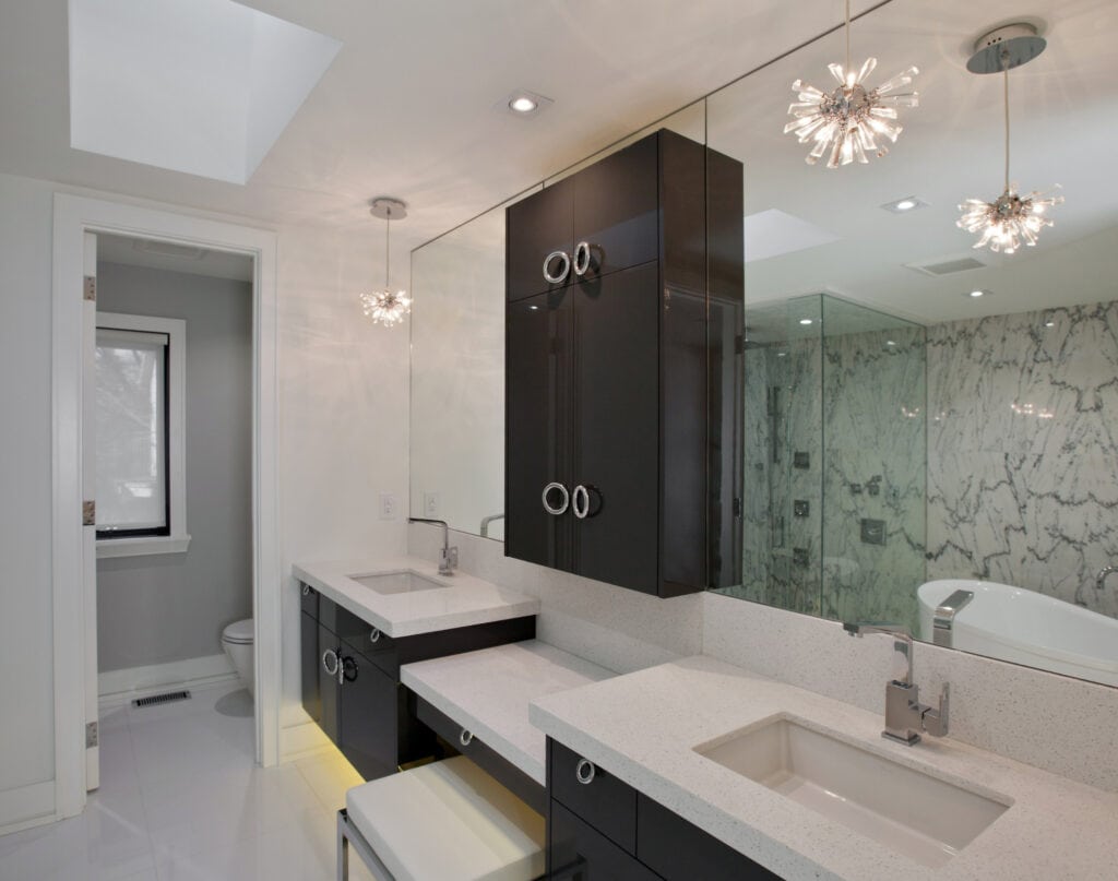 Modern luxury bathroom with black cabinetry, double sinks, marble wall accents, and contemporary lighting fixtures. Spacious, elegant, and designed for comfort and style.