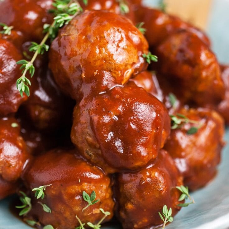 Juicy homemade meatballs covered in rich tomato sauce with fresh thyme garnishing, served on a plate for delicious comfort food.
