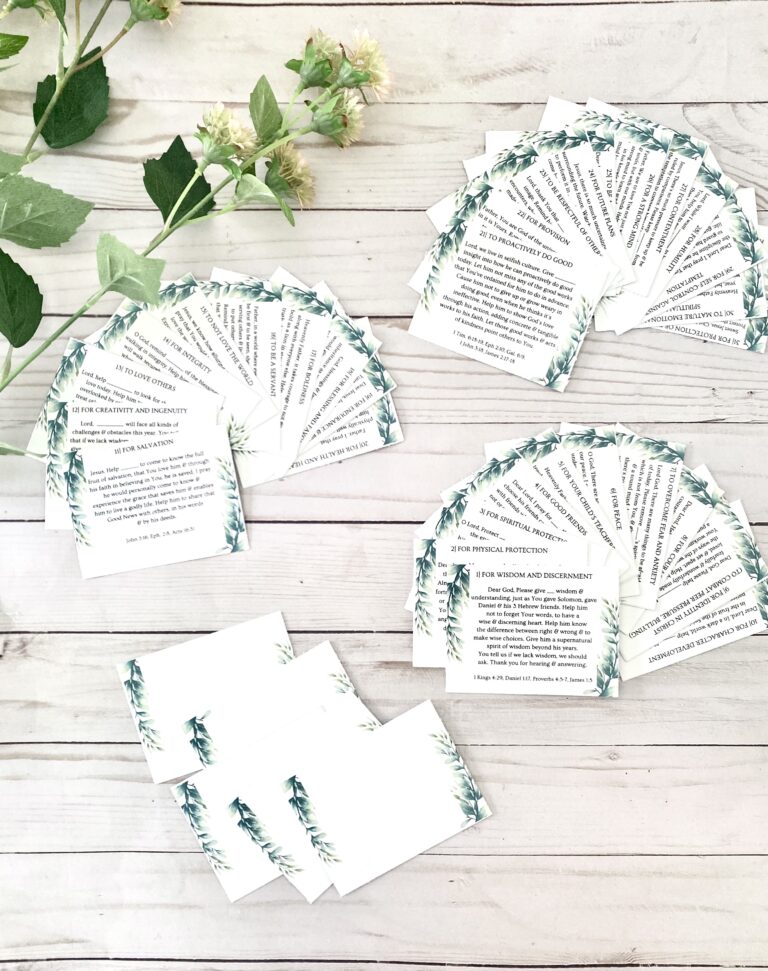 Authentic faith-based Bible scripture cards with inspirational messages on a white wooden surface, accented by a sprig of soft green and pink flowers, emphasizing spiritual growth and encouragement.