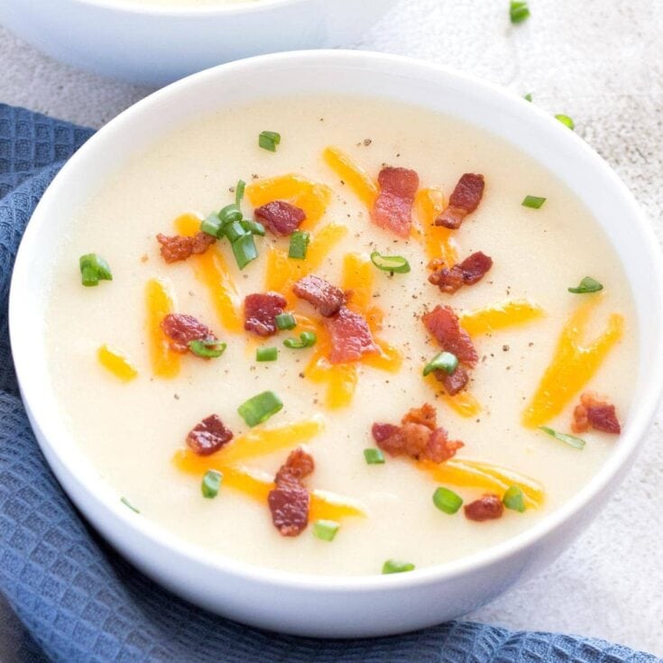 Creamy potato soup topped with crispy bacon, shredded cheddar cheese, and chopped green onions on a white bowl. Perfect comfort food for cozy meals.