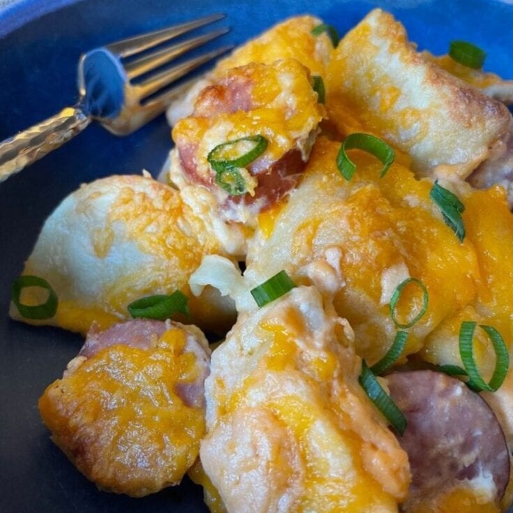 Scrambled eggs with melted cheddar cheese, chopped green onions, and breakfast sausage on a dark plate with a fork, showcasing a hearty breakfast dish.