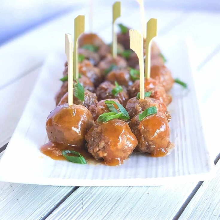 Savory glazed Asian-style meatballs garnished with green onions on a white platter.