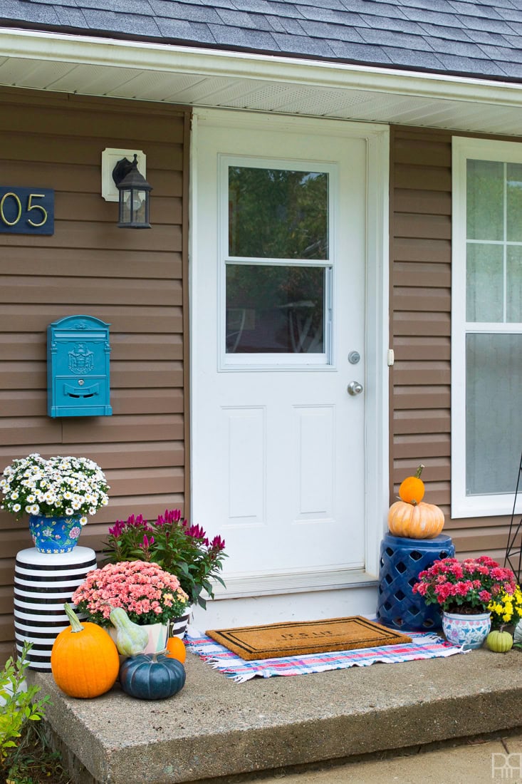 Colorful fall decorations with pumpkins, mums, and cheerful flowers at a welcoming front door for seasonal home decor.