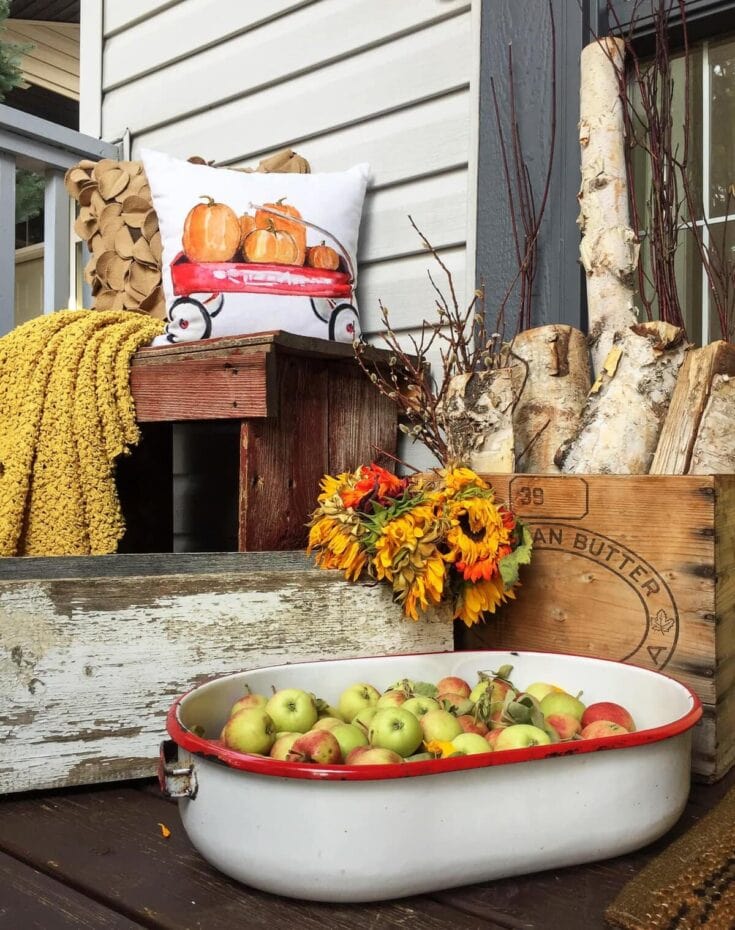Gourmet apples in a vintage enamel dish surrounded by rustic fall decor, sunflowers, and cozy textiles for a charming autumn harvest aesthetic.