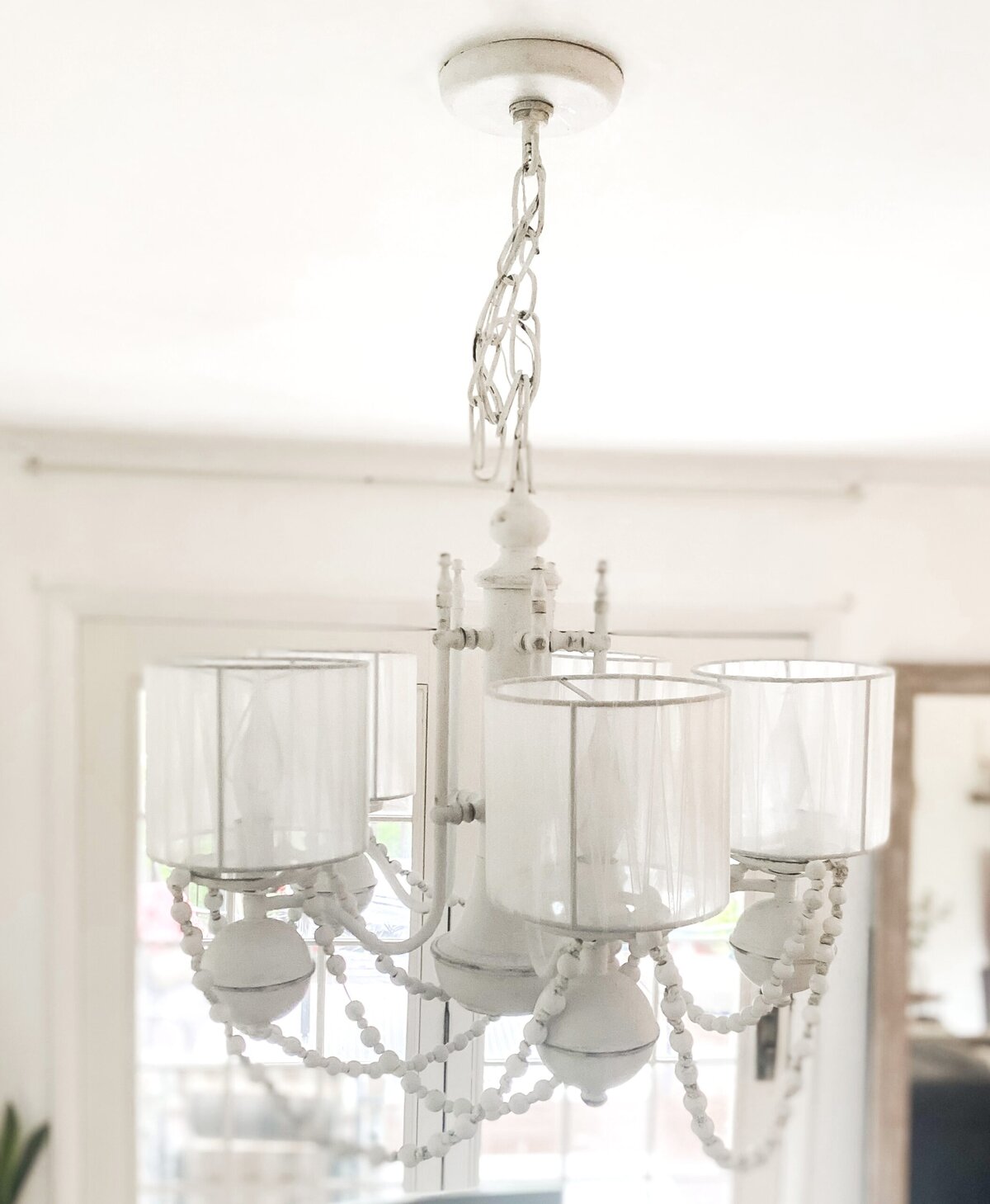 Elegant white chandelier with beaded accents, hanging from a minimalist ceiling mount inside a cozy home setting. Perfect for enhancing interior decor with vintage charm.