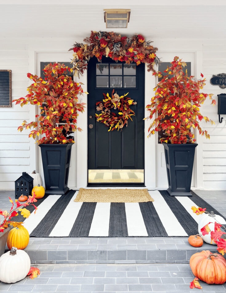 Vibrant fall foliage and pumpkins decorating a stylish front porch with a modern black door, creating a cozy autumn entrance with seasonal decor.