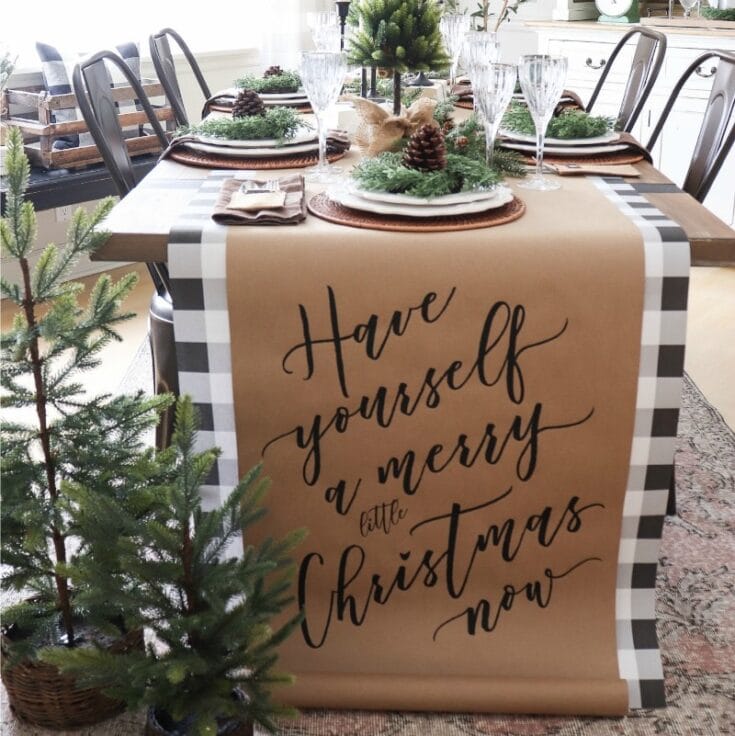 Festive Christmas table decorated with greenery, pinecones, and elegant glassware, featuring a rustic "Have yourself a merry little Christmas now" table runner for holiday celebration inspiration.