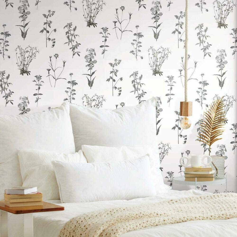 Delicate black and white floral wallpaper accent wall in a cozy, minimalist bedroom with white bedding and natural decor elements.