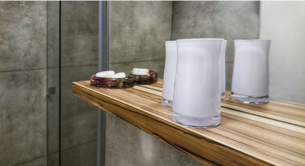 Clear drinking glasses and aromatic soap on a wooden shelf in a bathroom or spa setting, emphasizing relaxation and self-care.