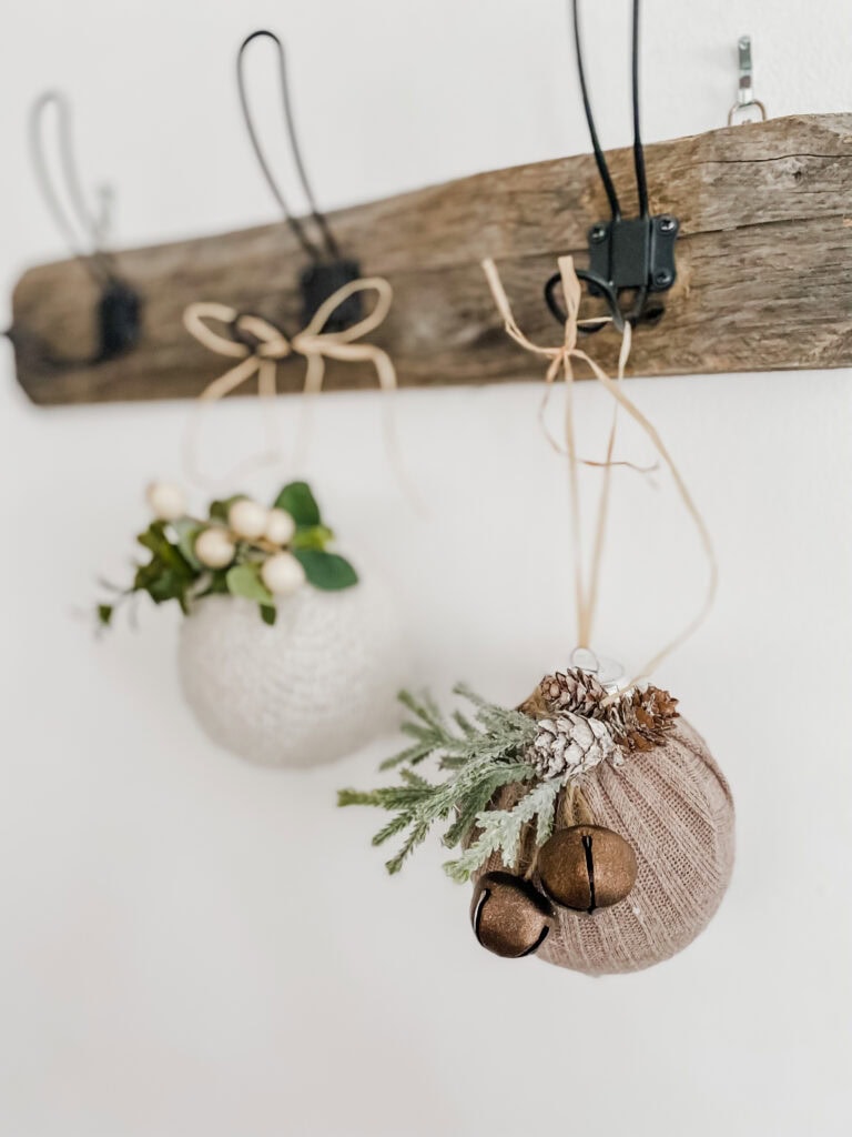 Soft rustic holiday ornaments hanging from a wooden wall hook with greenery, pinecones, and jingle bells, perfect for cozy seasonal decor and Christmas decoration ideas.