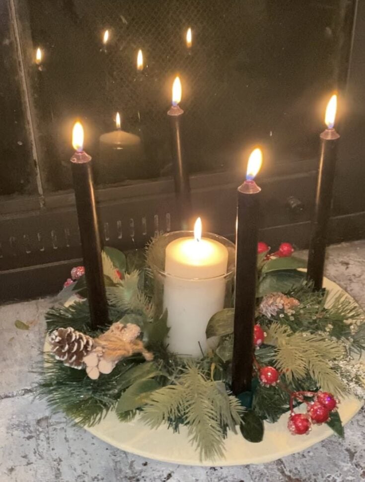 Candle centerpiece with four lit black candles, a white pillar candle, and festive holiday greenery including pinecones and red berries, perfect for cozy winter or Christmas decor.