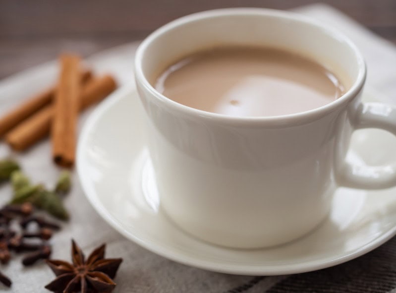 Creamy hot chocolate in a white mug on a saucer surrounded by cinnamon sticks and star anise, perfect for cozy winter moments.