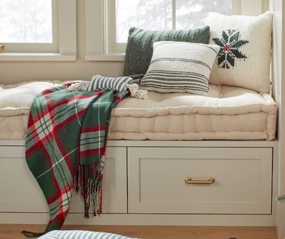Cozy window seat with layered pillows, a plaid blanket, and natural light, perfect for relaxing or reading, emphasizing comfort and home decor.
