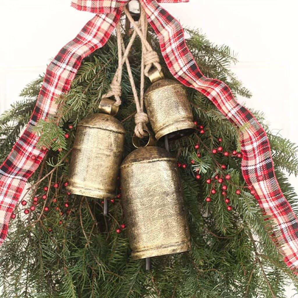 Shimmering gold bells decorated with red berries and greenery, adorned with a red and black plaid ribbon, perfect for Christmas holiday home decor or festive wreaths.