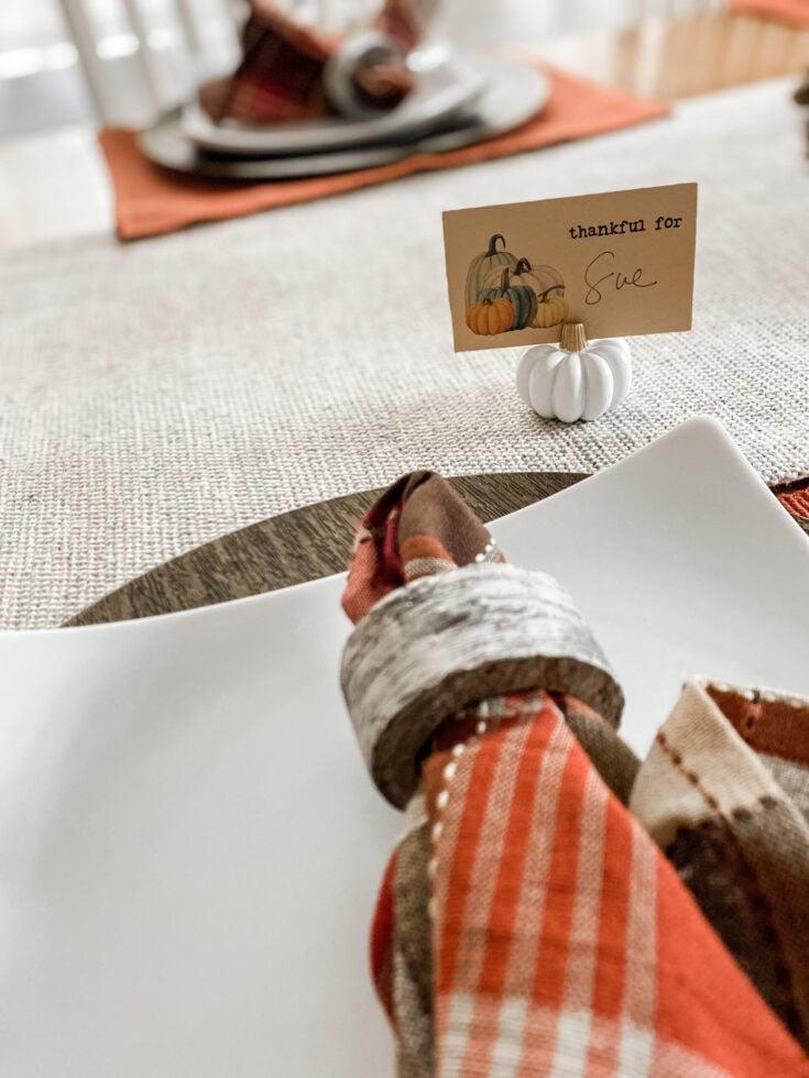 Pumpkin-themed place card on a dining table, autumn Thanksgiving decor, cozy seasonal centerpiece, fall table setting, and rustic holiday table decor.