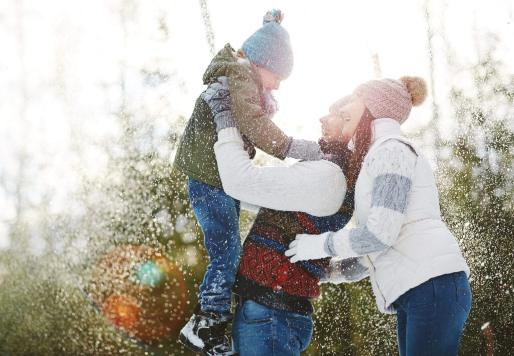 Family enjoying winter outdoor snow scene, children with parents in cozy winter clothing, smiling and playing in the snow near evergreen trees, capturing joyful holiday moment, A Hundred Affections.