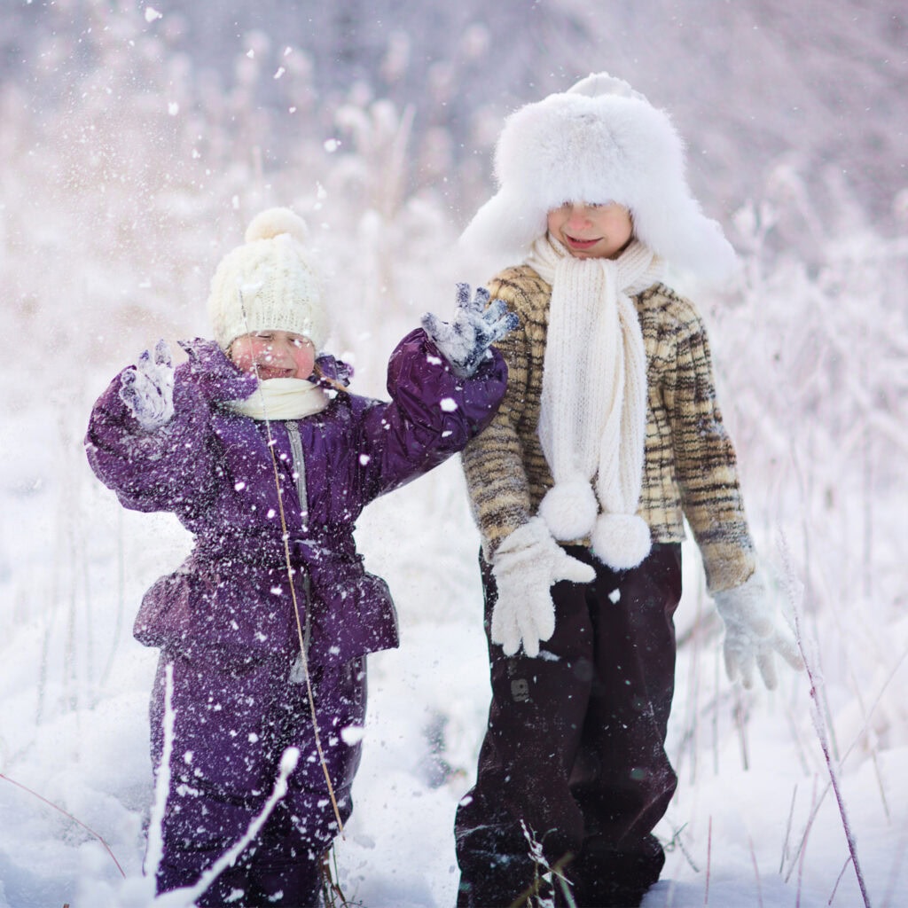 Playful children building snowmen in winter snow, wearing warm clothing, enjoying outdoor snow activities during cold weather, cozy winter apparel, outdoor family fun, snowy landscape, winter accessories, kids playing in snow, holiday winter season, outdoor winter adventure.