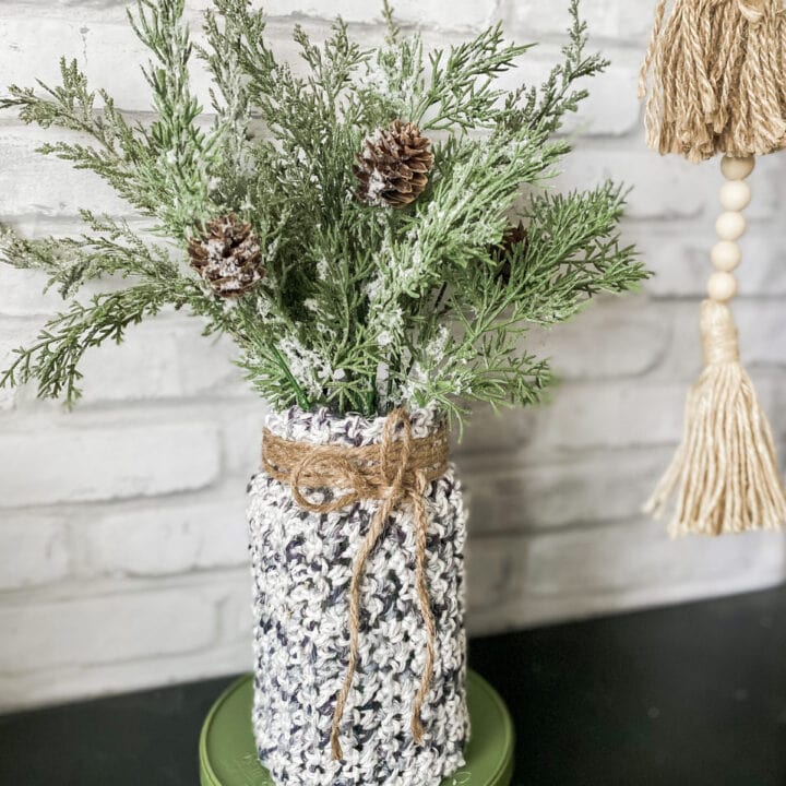 Aromatic greenery and pinecones displayed in a cozy, hand-knit fabric vase, perfect for festive home decor and Christmas celebrations.