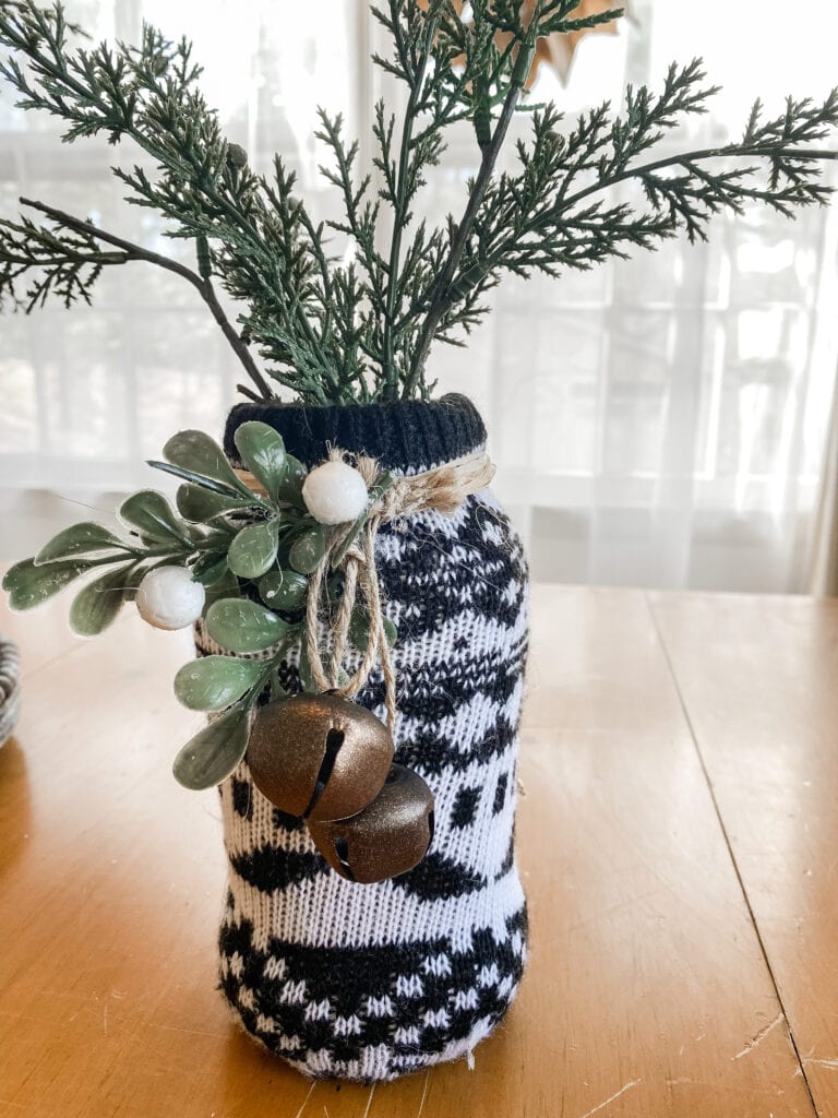 black and white sweater jar for winter craft with greens, bells and white berries