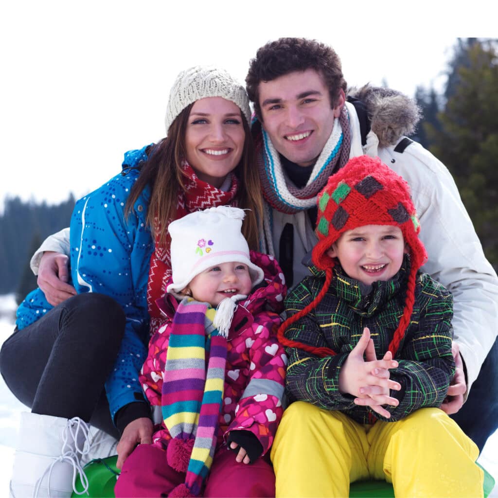Smiling family enjoying winter outdoors, dressed in colorful warm clothing, with snow-covered trees in the background, capturing joyful moments in a winter vacation setting.