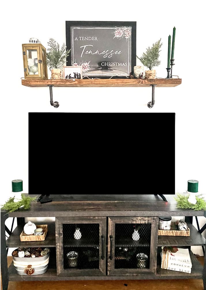 A festive Christmas decor setup with a chalkboard sign reading "A Tender Tennessee Christmas" on a rustic wooden shelf, surrounded by greenery, candles, and seasonal accents.