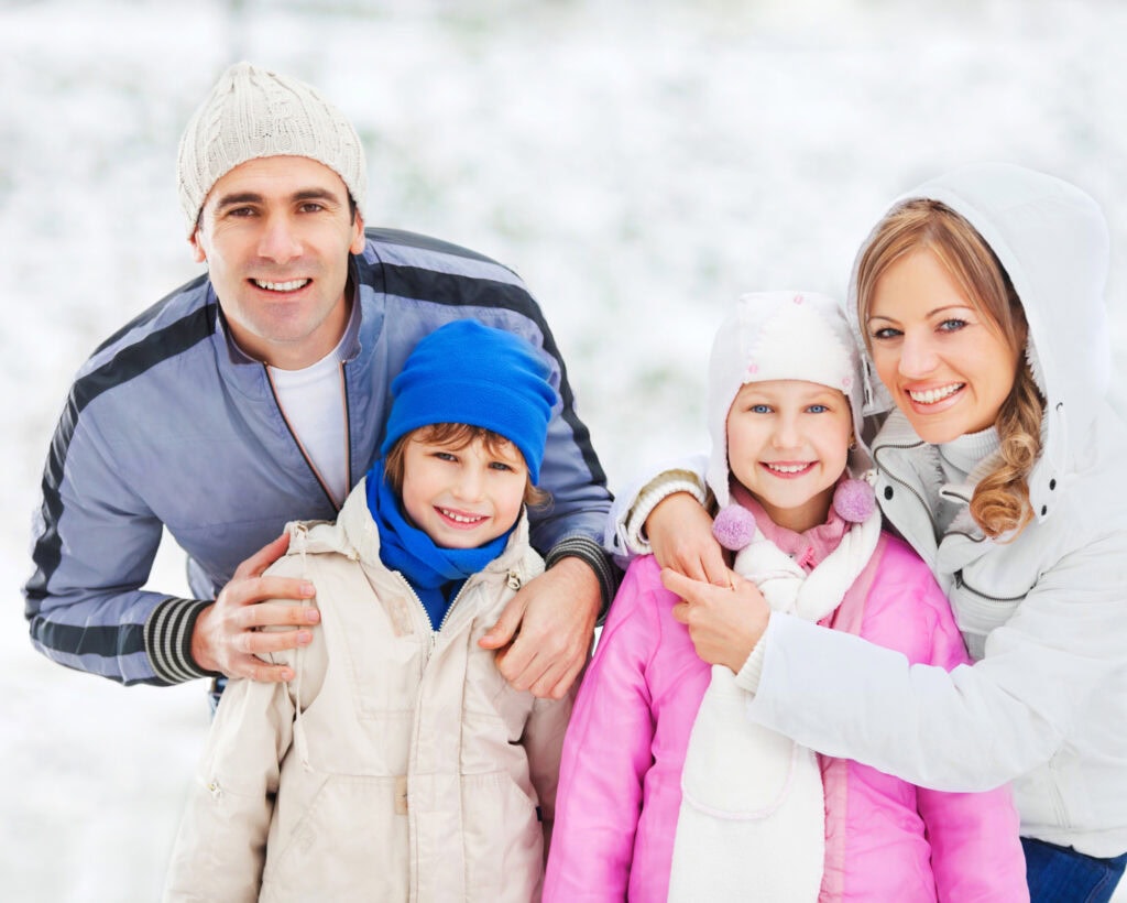 Happy family enjoying winter outdoors, kids in colorful jackets and hats, mom and dad smiling, snowy background, family bonding during cold weather.
