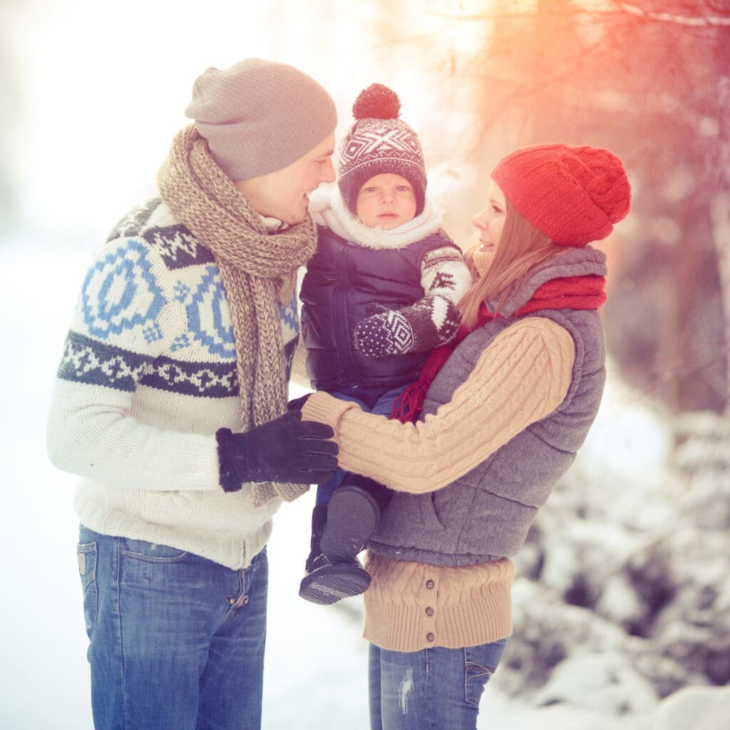 A happy family enjoying a winter day outdoors, wearing cozy knit winter clothing in a snowy landscape, representing love, warmth, and togetherness.