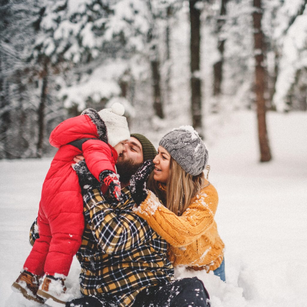 Joyful family snow day with parents and child playing in fresh winter landscape, wearing cozy warm clothing, celebrating together in snowy forest, capturing love, happiness, and family bonding during winter season.