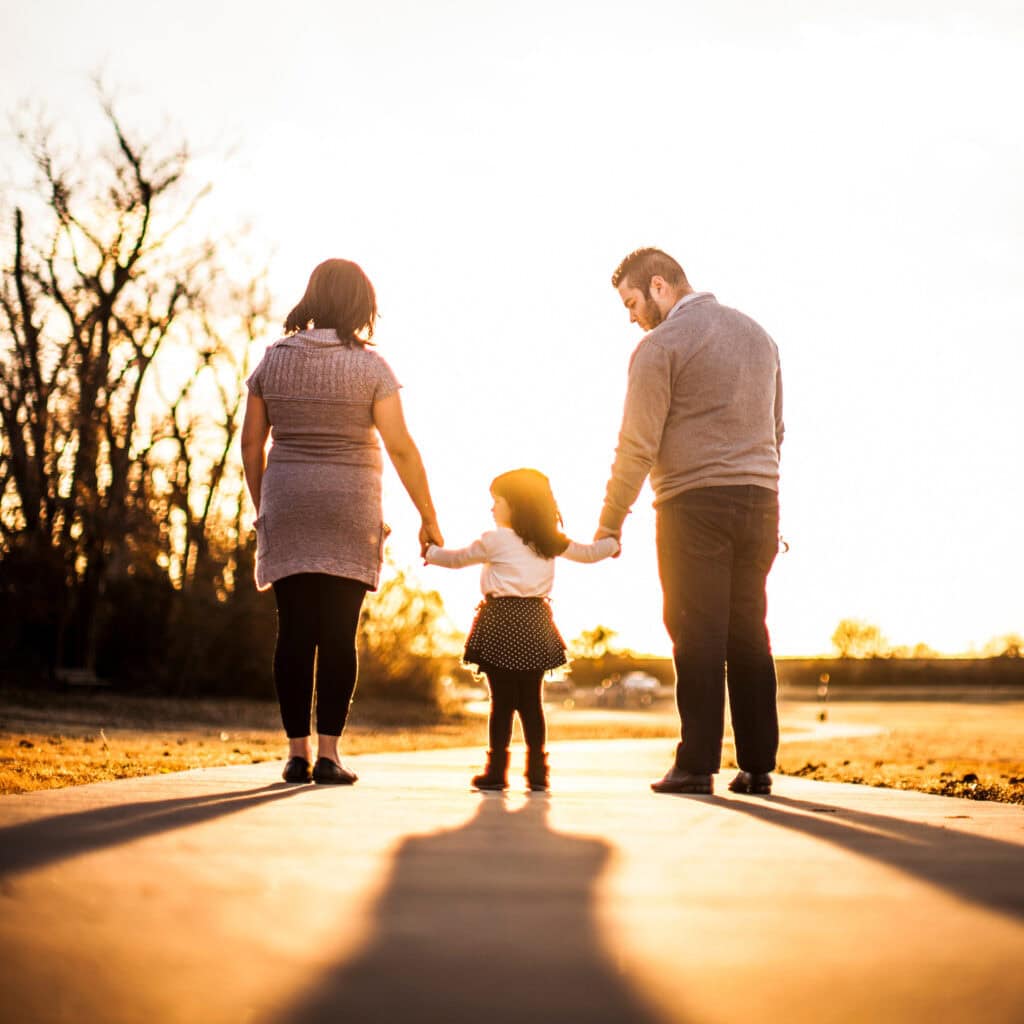 Warm family portrait of a mother, father, and young girl holding hands during sunset, capturing love and connection, perfect for family, parenting, and outdoor activity SEO.