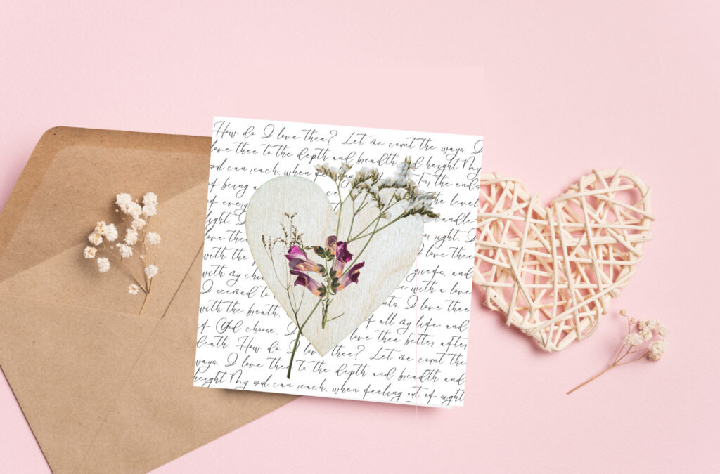 Delicate pressed flower love letter with handwritten script, pastel pink background, rattan heart decor, and dried baby's breath flowers for romantic wedding or anniversary themes.