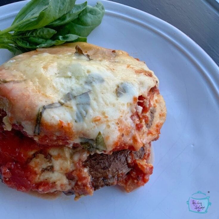 Savory baked eggplant parmesan with melted cheese, fresh basil garnish, and rich marinara sauce on a white plate. Perfect comfort food recipe for Italian-inspired dinners.