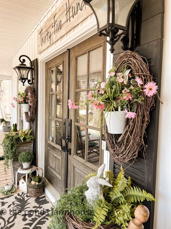 Rustic floral wreaths with pink daisies and greenery enhance the entryway of A Hundred Affections boutique. Charming outdoor decor creates a welcoming, farmhouse-inspired aesthetic for customers.