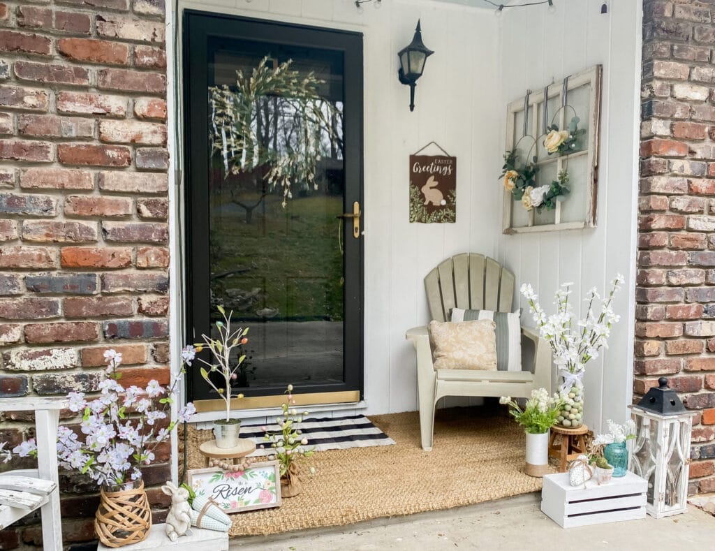 rustic farmhouse easter porch with chair and spring pillows, easter vignettes with easter egg trees, dogwood blossom, easter bunny and fabric carrots
