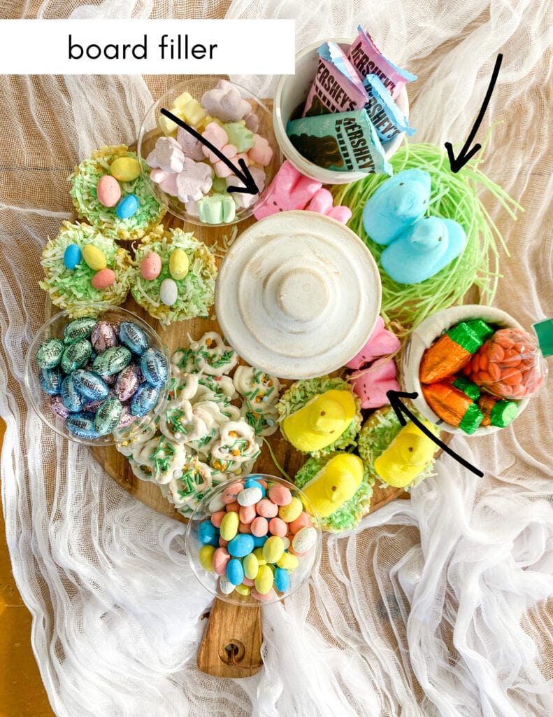 Colorful Easter candy and treat display with marshmallow chicks, chocolate eggs, and bunny-shaped sweets on a rustic wooden tray.