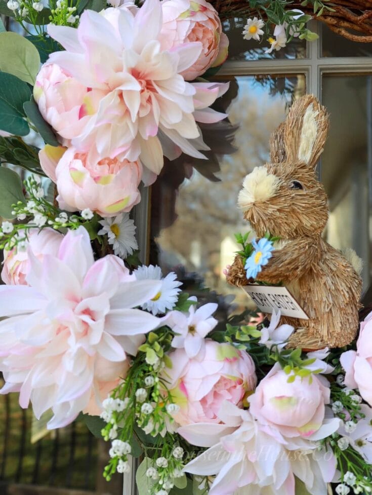 Bright pink and white peonies and daisies surrounding a rustic bunny figurine with a daisy in its paw, create a charming spring floral display perfect for Easter or spring decoration.