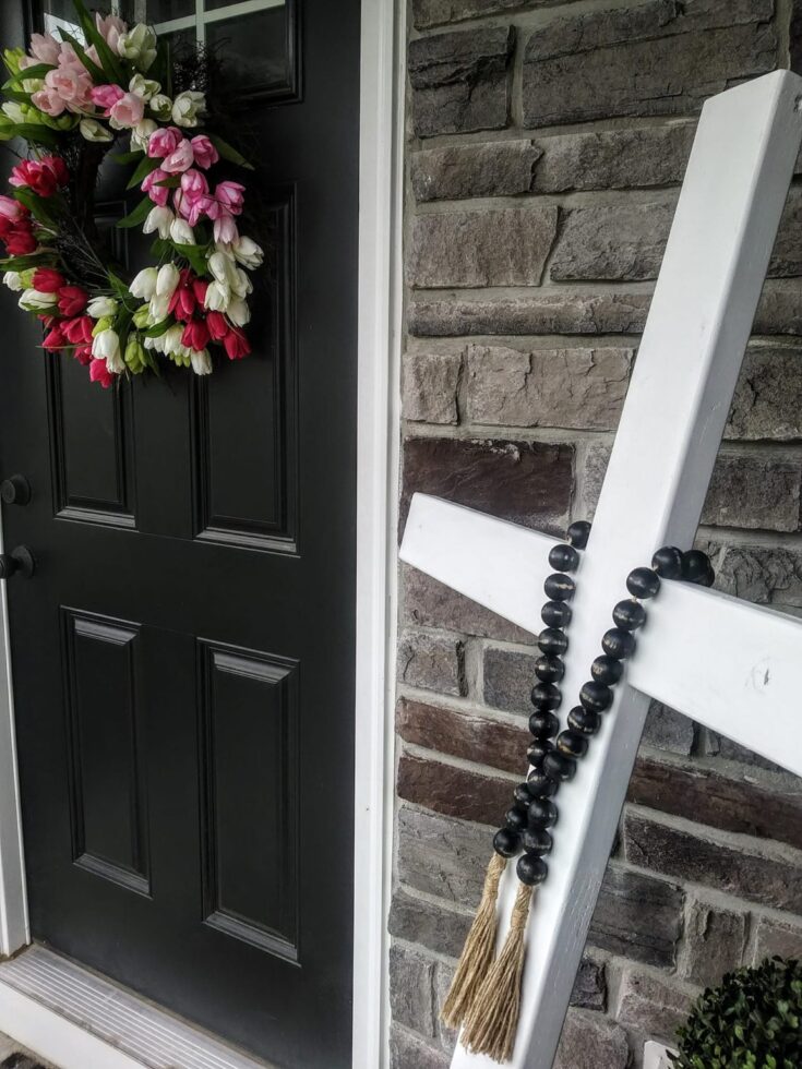 Beautiful front door with elegant floral wreath featuring pink, white, and red flowers, complemented by a white wooden ladder with black bead garland and tassels, creating a charming and welcoming entrance.