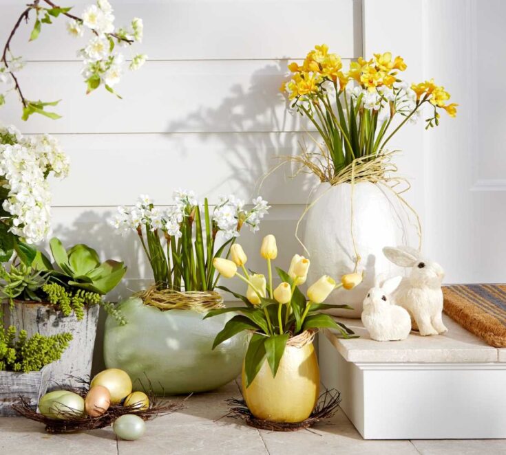Pastel Easter eggs and spring flower arrangements in white, green, and yellow vases with rabbit figurines, creating a festive and cheerful spring decor display.