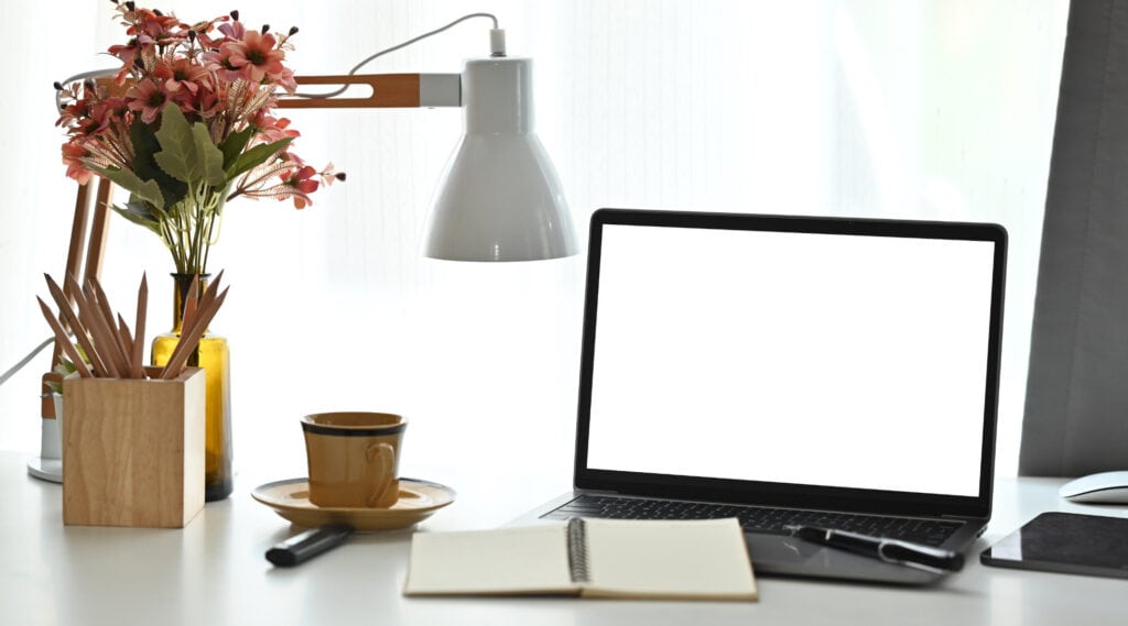 Colorful artificial flower arrangement in a glass vase on a modern workspace desk.