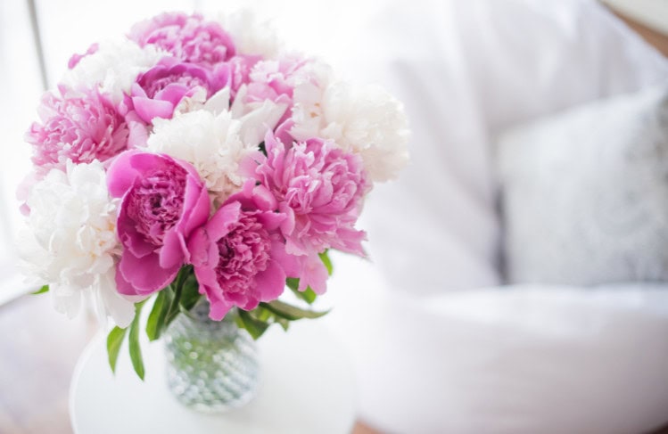 Vase of pink and white peonies flowers on a white table, elegant floral arrangement for home decor or special occasion.