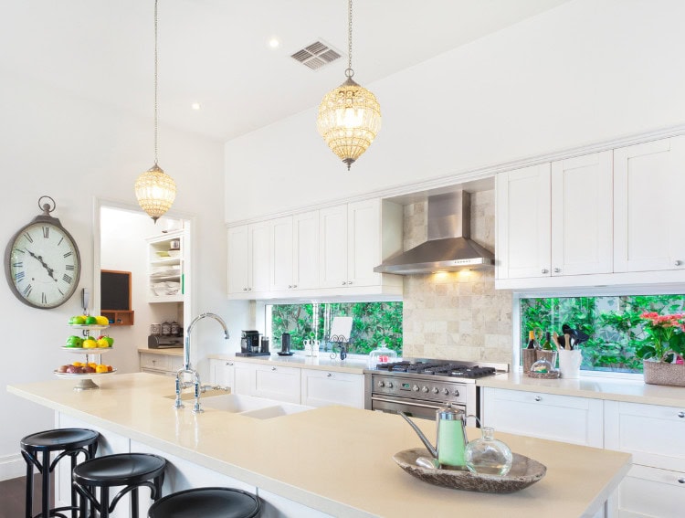 Bright modern white kitchen with large island, stylish pendant lighting, and lush greenery outside windows, perfect for a cozy and elegant home environment.