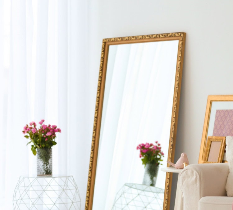 Bright living room decor featuring a large ornate gold-framed mirror, fresh pink flowers in a glass vase, and a cozy beige armchair with decorative pillows, creating an elegant and inviting atmosphere.